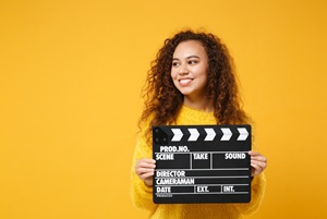 womancollegestudent_holdingvideoclapper_yellowbackground